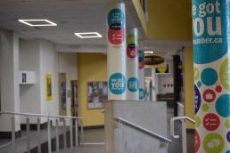 A photograph of an empty hallway at Humber college. Pillars with colourful dots and positive affirmations line the right side of the hallway.