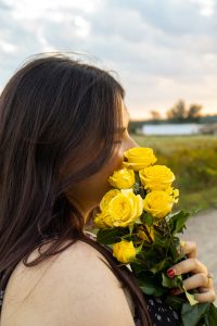 Girl smelling yellow flowers facing away from the camera.
