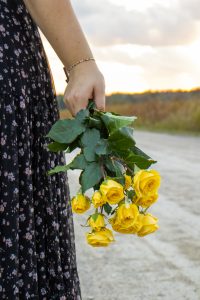 Girl holding flowers facing them towards the ground, like she is walking with them.