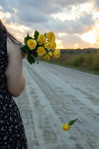 Girl walking away from the camera holding the flowers over her shoulder.